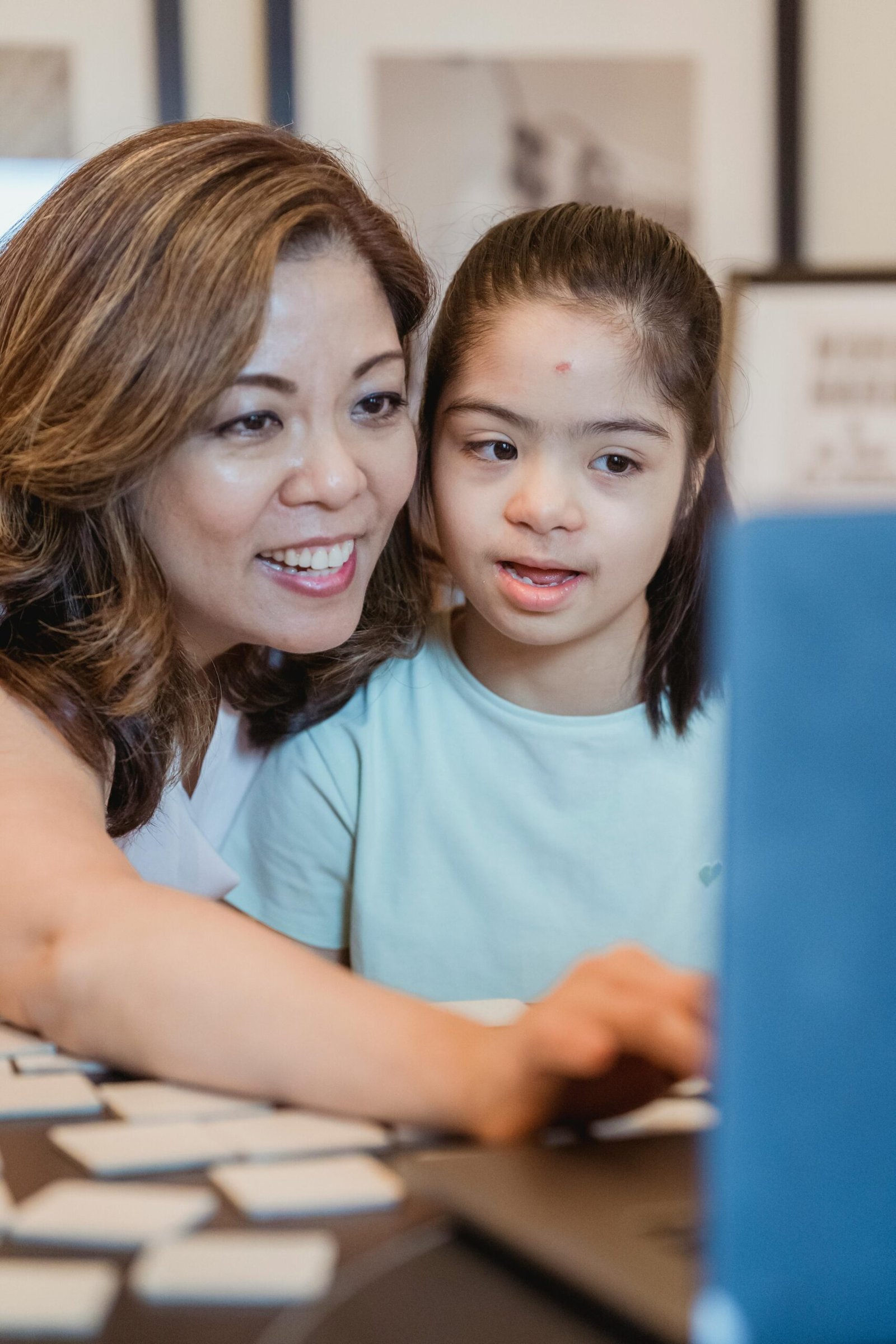 An adult and young girl with Down syndrome smiling and bonding indoors.